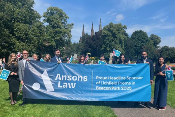A photo of Ansons staff with a banner announcing their sponsorship of Lichfield Proms in Beacon Park.