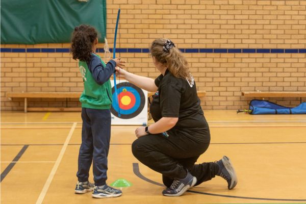 A photo of a young boy being taught soft archery.