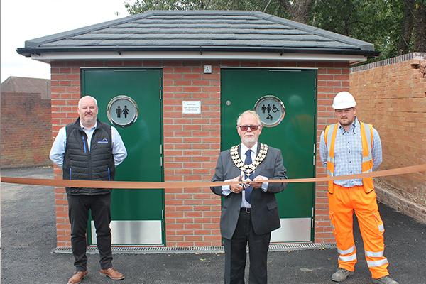 chairman cutting ribbon in front of toilets with a man either side of him