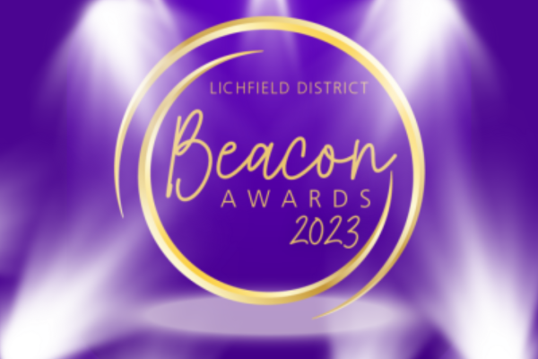A gold circle on a purple background with spotlights above and beneath. Lichfield District Beacon Awards 2023 in gold lettering within the gold circle.