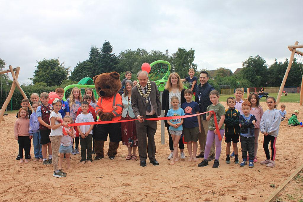 Colin Greatorex cutting the ribbon at Burntwood Park play area, with children, councillors Laura Ennis and Wai-Lee Ho and the parks mascot Ranger Ted.
