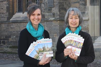 Two women from Visit Lichfield holding the guide and What's on brochures in front of St Mary's