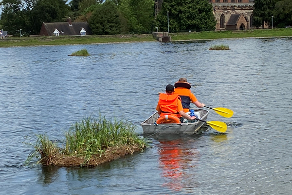 floating island being rowed out on water of Stowe Pool.