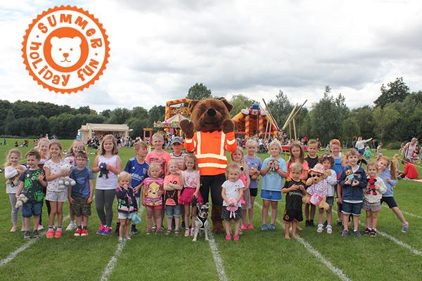 a teddy mascot surrounded by children and a dog in Beacon Park