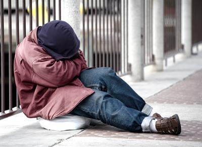 homeless man sitting on street with head in hands