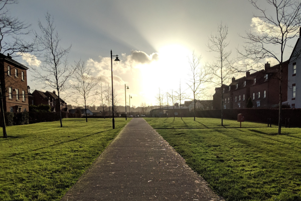 The sun sets across a long pathway flanked by grass on either side and mock Georgian style houses in Darwin Park Lichfield.