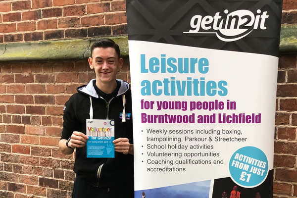 young man holds volunteering leaflet next to pull up volunteering banner