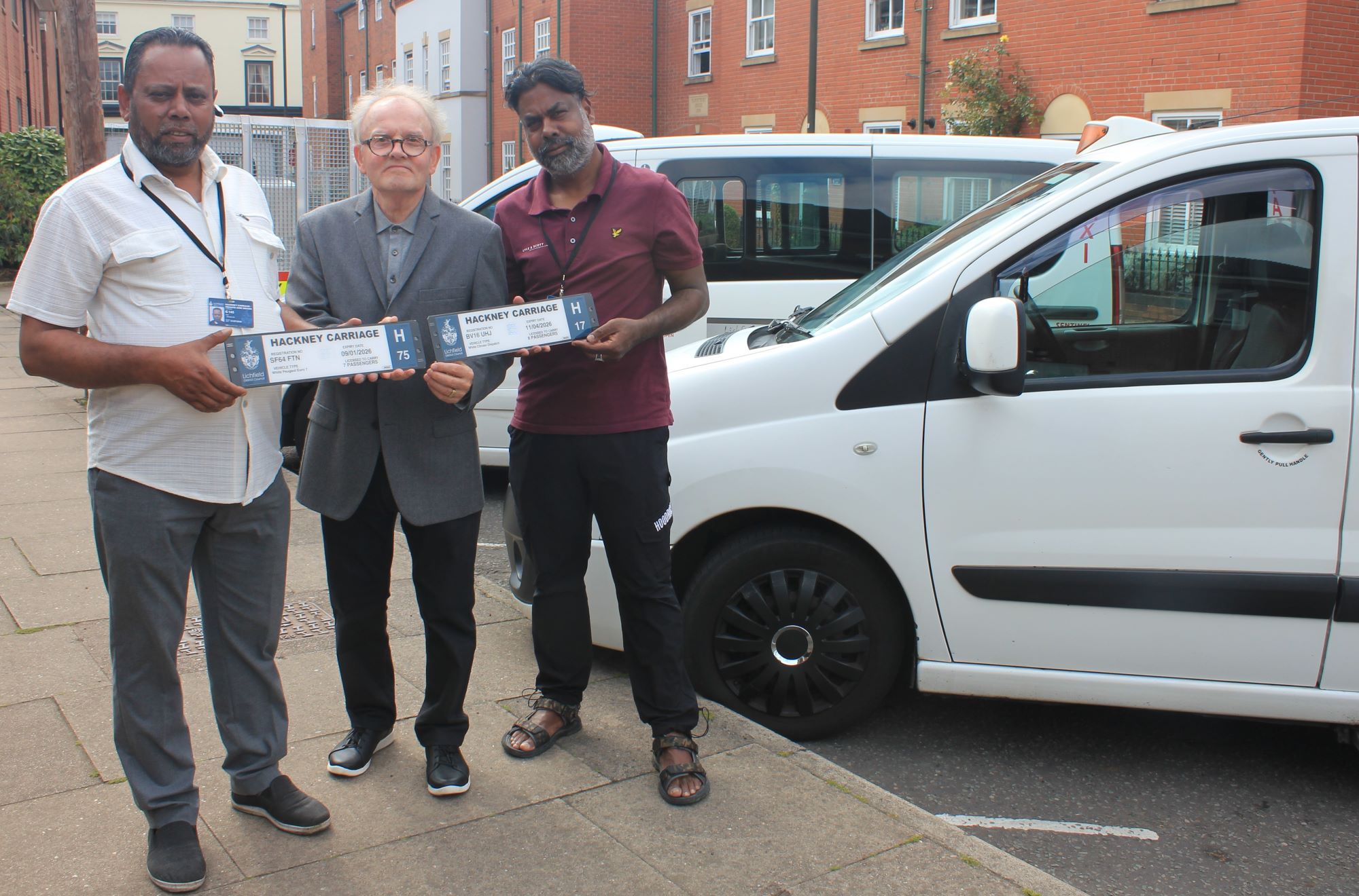 A photo of Councillor Brian Yeates issuing new plates to Jilkodar Ali (left) and Azizur Rahman (right), both of whom drive wheelchair accessible hackney carriages.