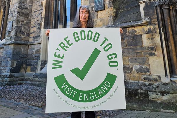 Woman holding We're Good To Go sign in front of historic building