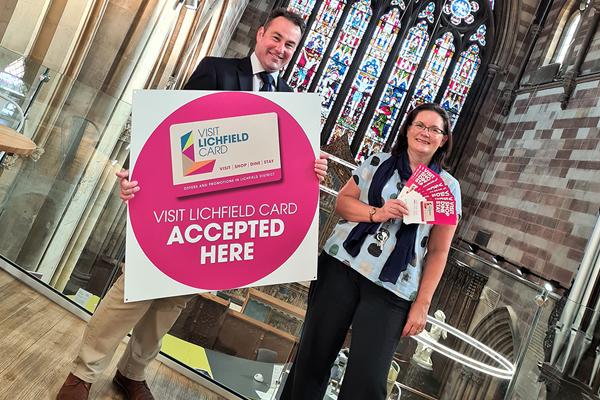 Iain Eadie holding a big sign that says Visit Lichfield card accepted here, stood next to Louise Flemming holding leaflets