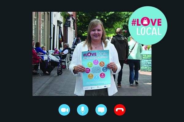 A woman holds a Love Local Poster in busy city street.