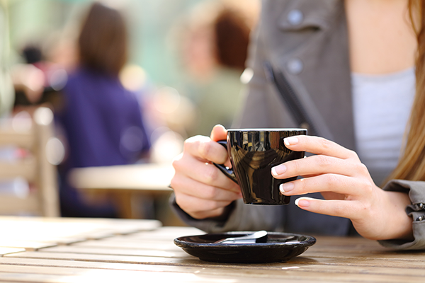 woman sat at outside cafe holds coffee cup