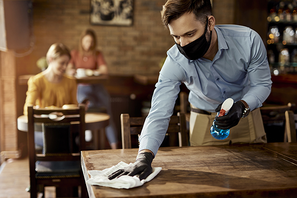 waiter wearing face mask cleaning a table